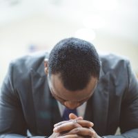 Lonely african-american male praying with his hands on the Bible with his head down